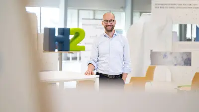 Interior shot: an employee standing in an office, in the background an H2 symbol